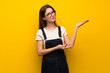 Woman over yellow wall extending hands to the side for inviting to come
