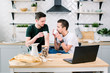 © sofiko14 - An image of Gay couple in kitchen. Attractive caucasian men drinking coffee and working on laptop computer at home kitchen, gay life concept
