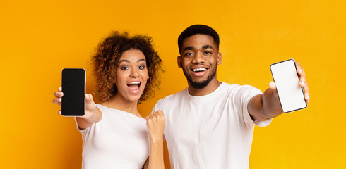Cheerful black couple showing blank smartphones at camera