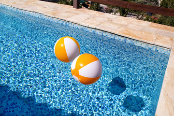 Two rubber air yellow white inflatable balls and toy for swimming pool in transparent blue water. Multi-colored beach balls floating on water in blue swimming pool for concept relax holiday travel.