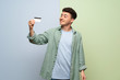 © luismolinero - Young man over blue and green background holding a credit card and thinking