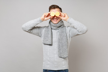 Wall Mural - Cheerful young man in gray sweater, scarf covering eyes with lemons isolated on grey background in studio. Healthy fashion lifestyle, people sincere emotions, cold season concept. Mock up copy space.