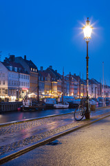 Wall Mural - Isolated street light with bicycle in blue twilight and view to embankment Nyhavn in Copenhagen in Denmark