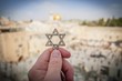 JERUSALEM, ISRAEL. February 15, 2019. Hand holding a Star of David, a Jewish religious symbol against the Western wall of the Jewish Temple in the Old city of Jerusalem. Judaism Zionism concept image.
