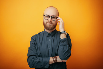 Wall Mural - Cheerful smiling young businessman touching his glasses, standing against yellow background