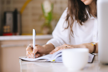 close up of a woman writer hand writing in a notebook at home in the kitchen