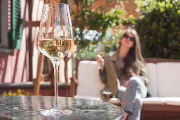 Wall Mural - glass of chilled white wine on table over young woman and Tuscany backgound