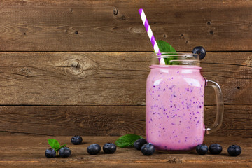 Wall Mural - healthy blueberry smoothie in a mason jar glass with scattered fruit over a rustic wood background