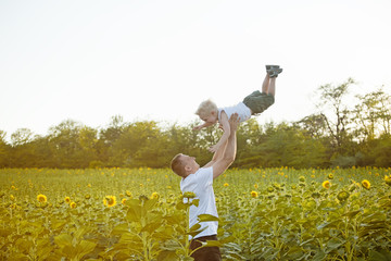 Wall Mural - Happy father throwing up a little laughing son on a green field of sunflowers