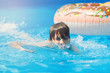 Happy cute little boy teenager lying on  inflatable donut ring with orange in swimming pool.  Active games on water, vacation, holidays concept. Chocolate donut. Cool fun summer holidays for children.