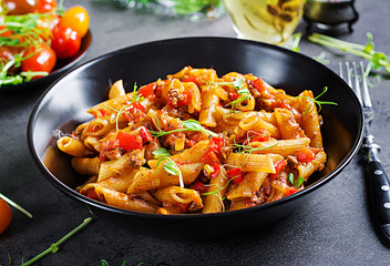 Wall Mural - Penne pasta in tomato sauce with meat, tomatoes decorated with pea sprouts on a dark table.