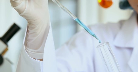 Wall Mural - Close up scene video of woman scientist dropping liquid into test tube in laboratory room.