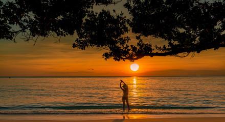 Wall Mural - Silhouette back view of sexy woman watching beautiful sunset at tropical paradise beach. Happy girl wear bikini and straw hat relaxing summer vacation. Holiday travel. Summer vibes. Peaceful life.