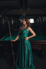 Young woman playing billiards in the dark billiard club