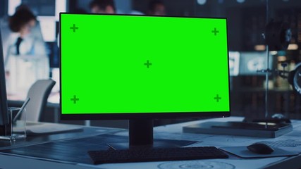On the Desk Standing Green Mock-up Screen Computer. In the Background Technology Development Laboratory with Scientists, Engineers Working on High Tech Electronics Industrial Design 