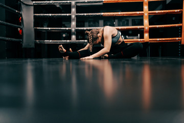 Wall Mural - Full length of Caucasian female boxer girl in sportswear stretching on floor in ring.