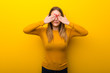 Young woman on yellow background covering eyes by hands. Surprised to see what is ahead
