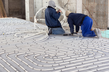 HVAC technicians working on underfloor heating system installation. Close up on water floor heating system interior of a new indoor swimming pool and SPA center. Plumbing pipes. Individual Heating.