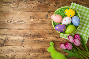 Easter holiday background with easter eggs in basket and tulip flowers on wooden table.