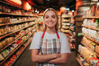 © estradaanton - Busy young woman stand in line between shelfs with pasta. She pose on camera and smile. Happy positive model.