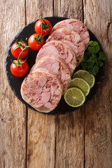 Delicious sliced Head cheese or brawn served with tomatoes, lime and cilantro closeup on a slate board. Vertical top view