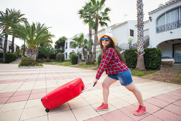 Wall Mural - Travel, tourism and holidays concept - funny young woman pulling her heavy suitcase