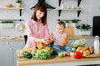 © sofiko14 - mother preparing salad for dinner and showing kid tomatoes in kitchen