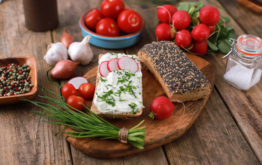 Wall Mural - wholemeal roll with quark and fresh chives, radish and tomatoes on a rustic wooden table - healthy breakfast with fresh herbs - close up