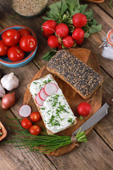 Wall Mural - wholemeal roll with quark and fresh chives, radish and tomatoes on a rustic wooden table - healthy breakfast with fresh herbs - close up