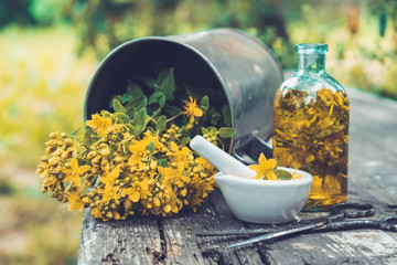 Wall Mural - St Johns wort flowers, oil or infusion bottle, mortar and big vintage metal mug of Hypericum plants on wooden board outdoors.