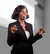 © TheVisualsYouNeed - young attractive and confident black African American business woman with headset speaking in auditorium at corporate training event or seminar giving motivation conference