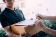 © wutzkoh - Delivery young man standing at the door of home and carrying parcels for young male to signing.