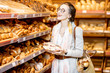 Young and elegant woman choosing sweet pastry, standing with bag in the bakery department of the supermarket