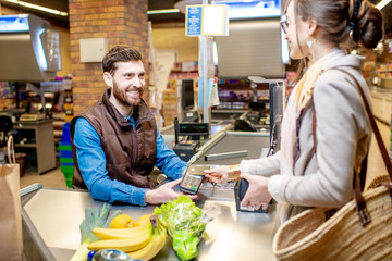 Young woman customer paying with a credit card for shopping at the cash register with cheerful cashier in the supermarket