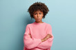 © wayhome.studio - Picture of angry Afro American young woman looks with grumpy facial expression, keeps arms folded, displeased with latest result of work, poses over blue background, expresses dissatisfaction