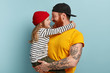 Children, parents, relationship and family concept. Attractive hipster father plays in free time with little daughter, carries on hands, have lovely talk, enjoy togetherness, stand over blue wall.