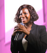 © TheVisualsYouNeed - confident black African American business woman with microphone speaking in auditorium at corporate event or seminar giving motivation and success coaching