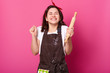 © sementsova321 - Baker woman holds baking rolling pin, wears brown apron, white t shirt. Young girl bends elbows and shouts yes with closed eyes, female maskes cake first time. Cook isolated on pink background.
