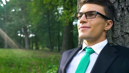 Cheerful business person sitting under big tree, unity with nature, happiness