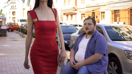 Fat man looking with delight at beautiful slim lady in red dress passing by