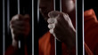 Desperate criminal holding jail bars feeling regret for committing crime closeup