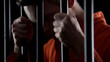 Convicted serial killer holding prison bars serving life sentence looking insane
