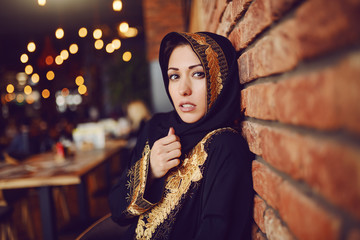 Wall Mural - Portrait of charming muslim woman with serious face sitting in cafeteria and looking at camera.