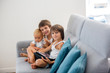 © Tomsickova - Sweet children, sitting on couch in sunny living room, playing on tablet