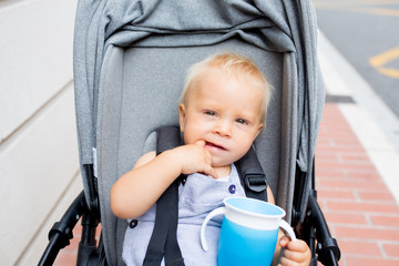 Sticker - Baby drinking water from special cup sitting in stroller outdoors