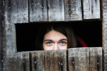 Woman locked in a wooden old barn, sad looks out the slit - upper half of face and eyes.