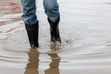 A Man In Rubber Boots Walks Through A Muddy Puddle