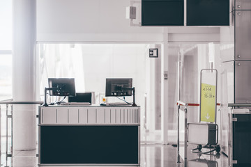 Wall Mural - An empty gate of a modern airport terminal with computer monitors on the counter, information screens on the top, baggage gauge, and the bright corridor leading to the airplane to boarding