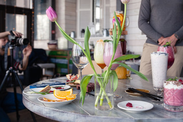 Food stylist and photographer decorate, preparing to shoot various cocktails, milkshakes, smoothies, flower tulips vase on table. Concept professional photography, photosession new menu, freelance