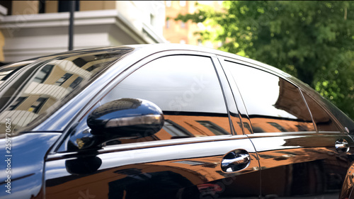 Zdjęcie: Luxury car with tinted glass standing at parking, reflection of businessman Luxury car with tinted glass standing at parking, reflection of businessman